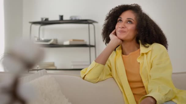 Smiling pretty ethnic African American gen z girl dreamy relaxed woman inspired relax on home couch imagine dream in apartment enjoy dreaming in morning weekend leisure relaxing resting in living room - Footage, Video