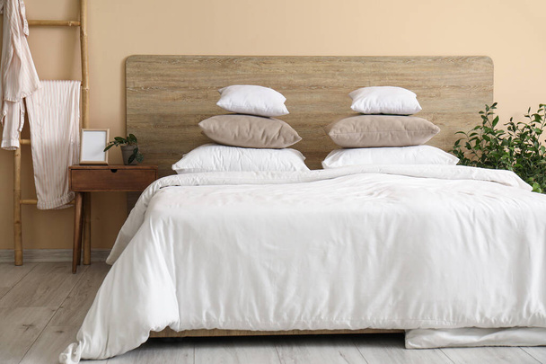 Cómoda cama con almohadas blancas, mesita de noche y planta de interior en el dormitorio - Foto, Imagen
