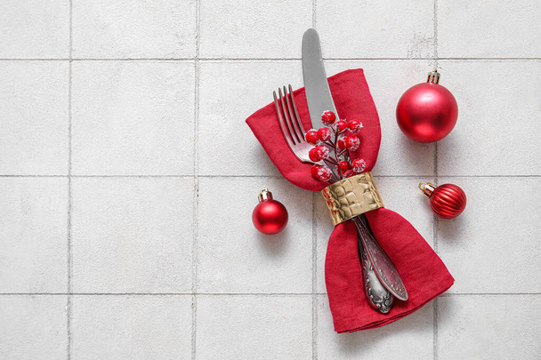 Servilleta roja con cubiertos y bolas de Navidad sobre fondo de baldosas blancas - Foto, imagen
