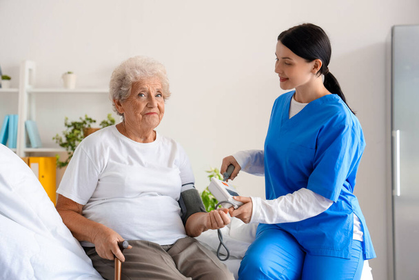 Krankenschwester misst Blutdruck von Seniorin im Schlafzimmer - Foto, Bild