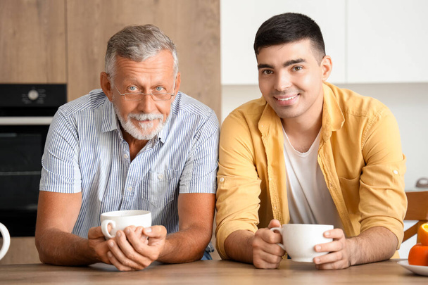 キッチンでお茶を飲んでいる息子とシニア男性 - 写真・画像