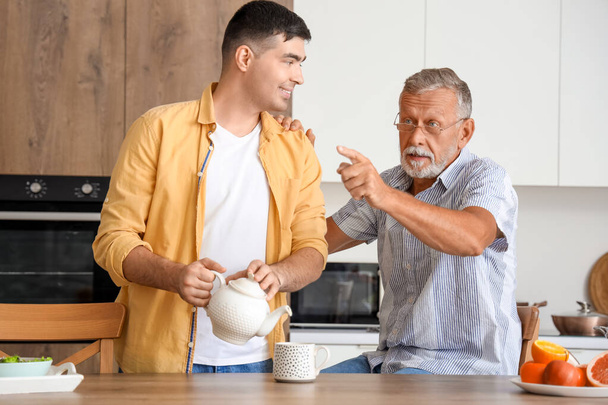 Nuori mies kaataa kuumaa teetä isälleen keittiössä - Valokuva, kuva