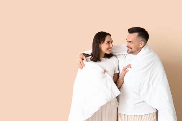 Молодая пара с мягким одеялом на бежевом фоне - Фото, изображение