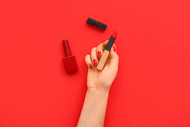 Vrouwelijke hand met stijlvolle rode manicure houden lippenstift en nagellak fles op kleur achtergrond - Foto, afbeelding