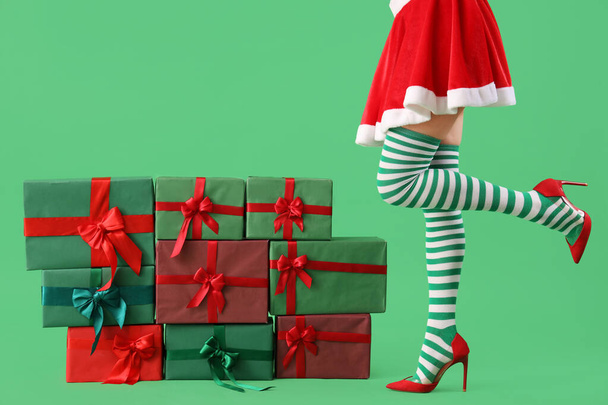 Sexy junge Frau in Weihnachtsstrümpfen mit Stapel von Geschenken vor farbigem Hintergrund - Foto, Bild