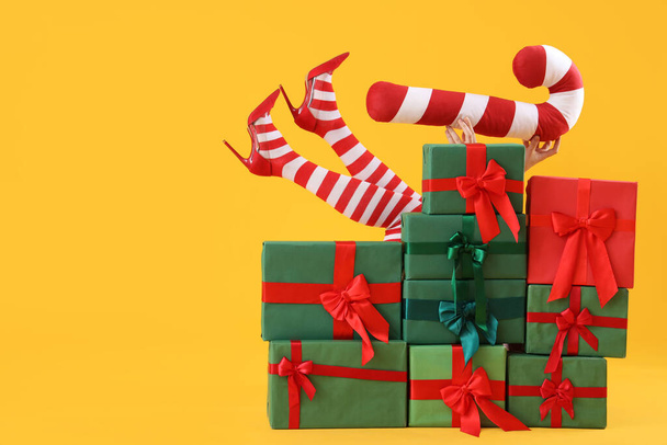 Frau in Weihnachtsstrümpfen mit Kissen hinter einem Stapel Geschenke auf gelbem Hintergrund - Foto, Bild