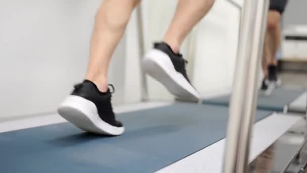 Kardiyak stres testi sırasında koşu bandında koşan bir adamın bacaklarının dikiz görüntüsü. - Video, Çekim