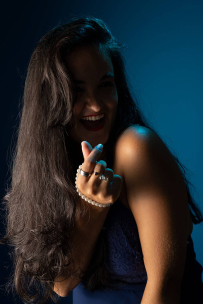 Porträt einer schönen Frau mit schwarzen Haaren, fröhlich, selbstbewusst, in einem blauen Kleid, die in die Kamera blickt. Vereinzelt auf dunkelblauem Hintergrund. - Foto, Bild