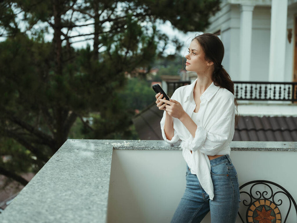 Woman on the balcony of the house with phone beautiful smile on a day off, beautiful view of nature in the mountains, lifestyle vacation in the hotel. High quality photo - Photo, Image