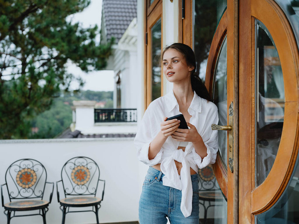 Mulher na varanda da casa com telefone belo sorriso em um dia de folga, bela vista da natureza nas montanhas, férias de estilo de vida no hotel. Foto de alta qualidade - Foto, Imagem