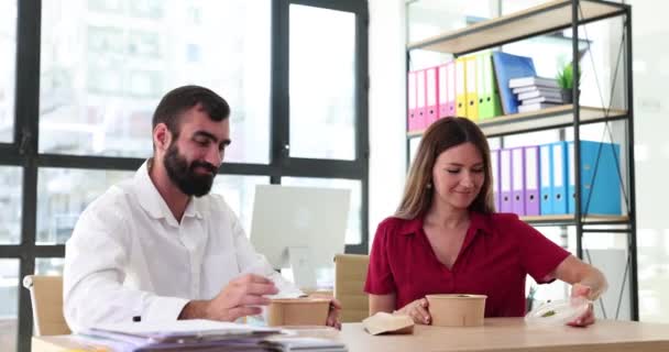 Ελκυστική νεαρή γυναίκα και ο άνθρωπος απολαμβάνει το φαγητό κατά τη διάρκεια του διαλείμματος γεύμα στο γραφείο. Γυναίκα υπάλληλος που κρατά το κουτί στο χώρο εργασίας με συνάδελφο στο γραφείο - Πλάνα, βίντεο