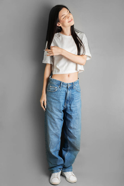 Full length portret van een jonge tiener meisje in een wit T-shirt en jeans. - Foto, afbeelding
