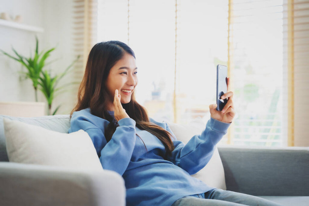 Happy young asian woman relax on comfortable couch at home texting messaging on smartphone, smiling girl use cellphone, chatting online message, shopping online from home - Photo, Image