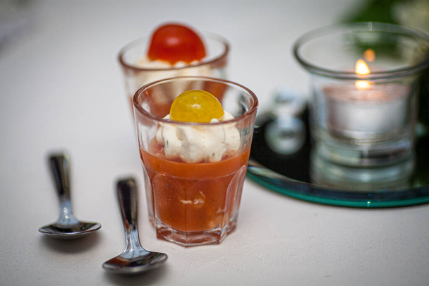 Bu resimde bir bardak kremalı domates çorbası, bir tutam krema ve bir parça da vişneli domates garnitürlü zarif bir aperatif sunumu yer alıyor. Çorba bardakta servis edilir. - Fotoğraf, Görsel