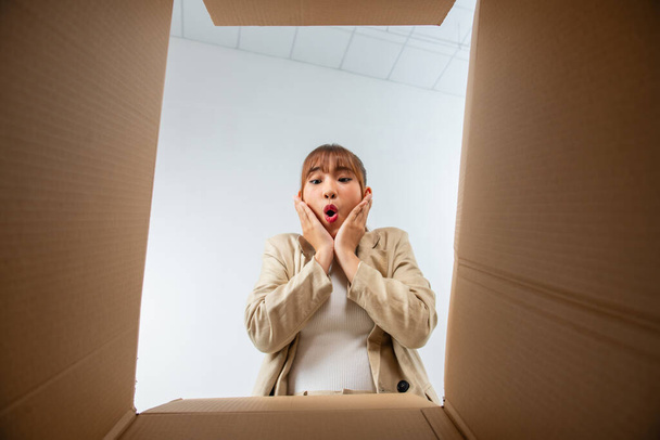 Alegre mujer joven asiática abriendo caja de cartón o paquete y mirando dentro - Foto, Imagen