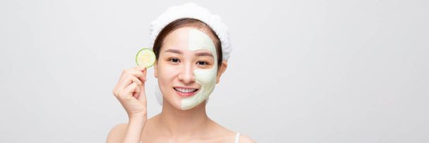 Mladá asijská krásná žena drží čerstvou okurku, bílá maska kosmetické na obličeji, prapor široký - Fotografie, Obrázek