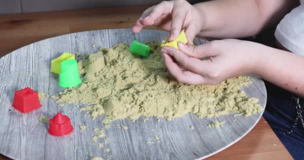 A young girl, is sitting at table, engrossed in play with kinetic sand, using her hands to sculpt and create various shapes and molds, expressing her creativity and imagination. - Footage, Video