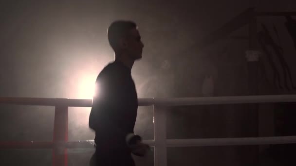 ボクシングリングでロープをジャンプする若いボクサー,煙の中の彼のシルエット. ドラマティック。 コピースペース - 映像、動画