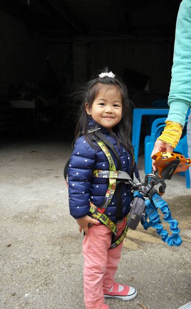 Çocuk, küçük Avrasyalı kız Çin ve Fransızca karışımı, kameraya bakıyor, ağaç tırmanma ekipmanıyla. - Fotoğraf, Görsel