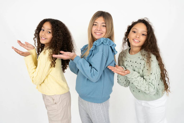 Három fiatal, gyönyörű, multiracionális lány, akik nyitott tenyérrel mutogatnak a másolótérre, és vidáman mosolyogó hirdetéseket mutatnak be. - Fotó, kép