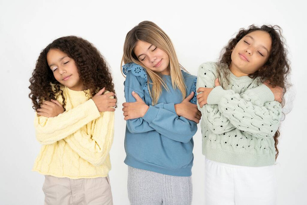 Τρία νεαρά όμορφα πολυφυλετικά κορίτσια αγκαλιάζουν τον εαυτό τους χαρούμενο και θετικό, χαμογελώντας με αυτοπεποίθηση. Αυτοαγάπη και φροντίδα - Φωτογραφία, εικόνα