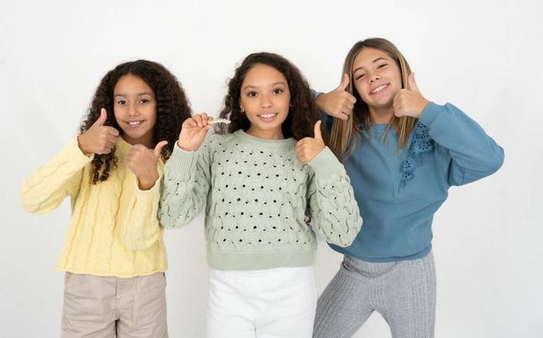 目に見えない勇気を持ち,親指を上げてこの新しい治療法を推奨する3人の美しい多人種間の少女. 歯科医療コンセプト. - 写真・画像