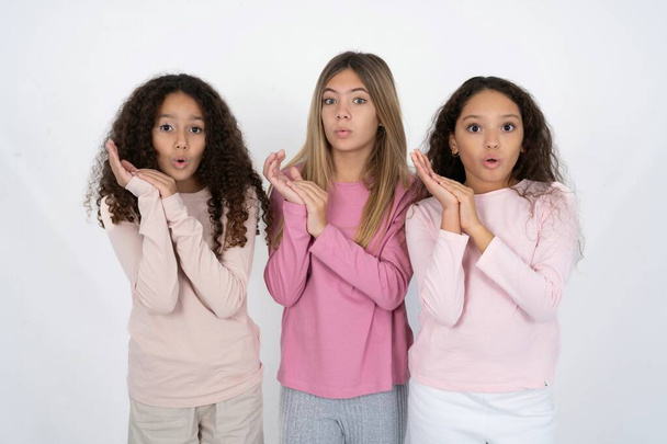 Surprised emotional Three young beautiful multiracial kid girls rubs palms and stares at camera with disbelief - Photo, Image