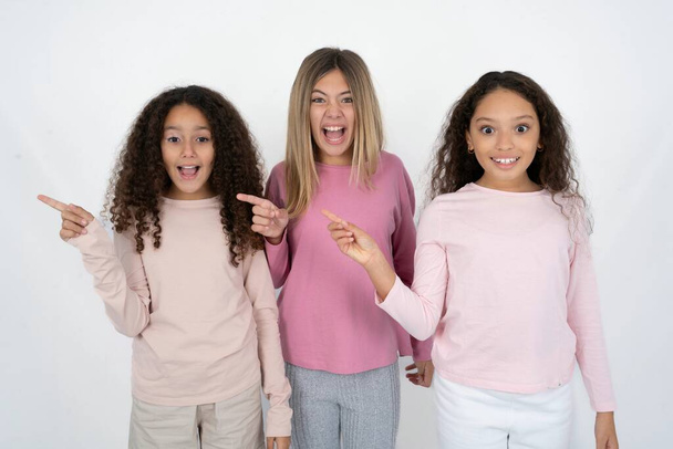 Τρία νεαρά όμορφα πολυφυλετικά κορίτσια δείχνουν στην άκρη σε κενό χώρο αντιγραφής. Έννοια της προώθησης και της διαφήμισης - Φωτογραφία, εικόνα