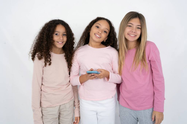 Drie mooie, multiraciale meisjes maken kopieerruimte. Mobiele telefoon gebruiken, sms-bericht typen - Foto, afbeelding