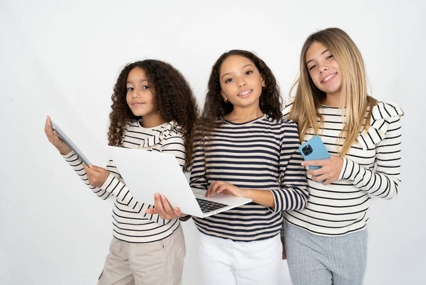 Adorable Tres chicas jóvenes y hermosas niños multirraciales sosteniendo un dispositivo moderno - Foto, imagen