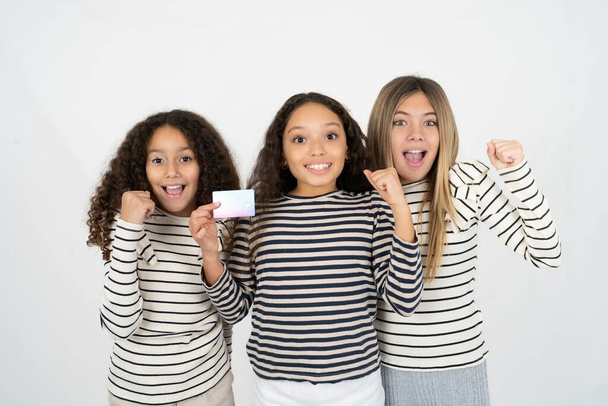 Zdjęcie szczęśliwego wrażenia Trzy młode, piękne, wielorasowe dziewczęta trzymają pięść z kartą kredytową. Obchodzone - Zdjęcie, obraz