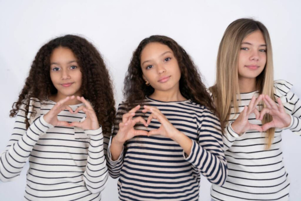 Serieuze multiraciale groep van meisjes vrienden tonen harten met handen over witte studio achtergrond  - Foto, afbeelding