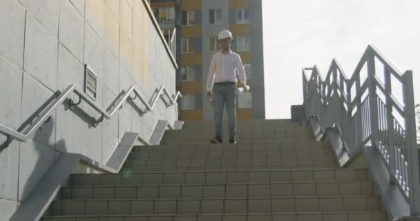 Архитектор спускается по лестнице, тщательно рассматривая планы строительства. Эксперт следит за точностью и тщательностью на каждом этапе проекта - Кадры, видео