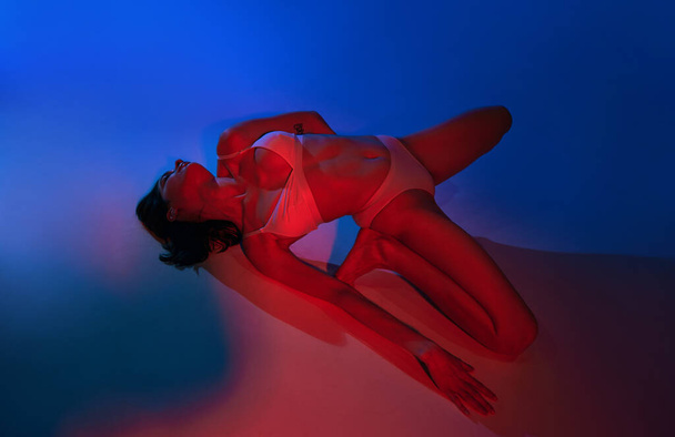 Elegance and neon vibrancy. Young woman posing in underwear against studio background in energetic glow of neon light. Concept of art, female health, wellness, self-expression. - Photo, Image