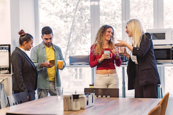Οι επιχειρηματίες μιλούν ενώ χαλαρώνουν κατά τη διάρκεια του διαλείμματος καφέ στο γραφείο. Επιχειρηματική έννοια. - Φωτογραφία, εικόνα