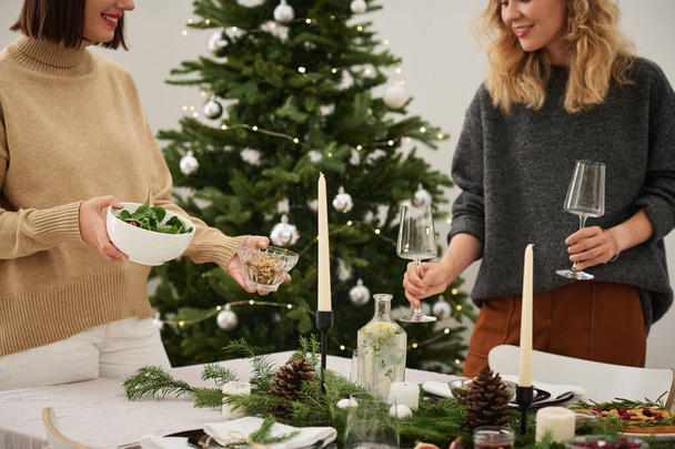 İki beyaz kadın Noel masasında aperatifler ve sofra takımı için yer seçiyor. - Fotoğraf, Görsel