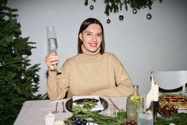 Souriant femme caucasienne posant avec boisson dans sa main assis à la table au dîner de Noël - Photo, image