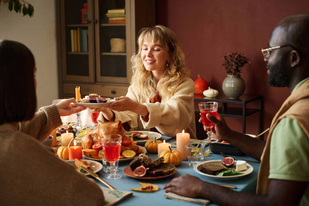 blank meisje passeren bord met voorgerecht naar haar vriend op thanksgiving feest - Foto, afbeelding