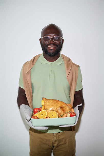 カメラで微笑む家禽や野菜でトレイと立っている若いアフリカ系アメリカ人男性 - 写真・画像