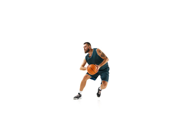 Basketball professional in uniform, exhibiting flawless dribbling technique and executing impressive slam dunk against white background. Concept of sport, hobby, active lifestyle. Copy space, ad - Photo, Image