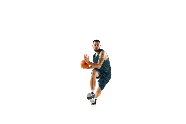 Professional basketball player in uniform, engaged in focused training session before match against clean white background. Concept of sport, hobby, active lifestyle, power and strength. Copy space. - Photo, Image