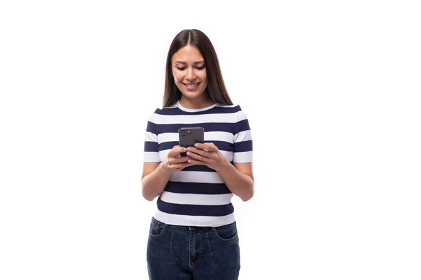 jong brunette europees dame van slank gebouwd gekleed in een gestreept zomer t-shirt chatten op een smartphone. - Foto, afbeelding