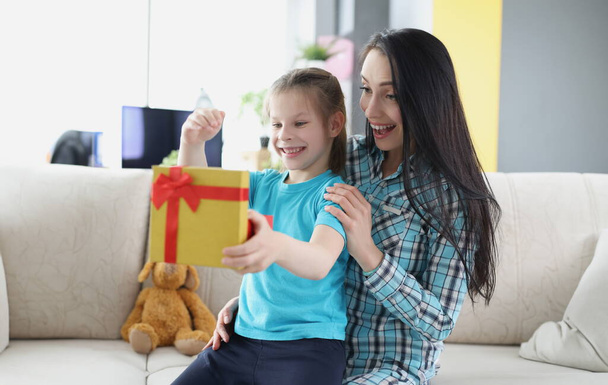 Маленька щаслива дівчинка сидить на колінах матері і відкриває подарункову коробку вдома. Вибір подарунків для дитячої концепції
 - Фото, зображення