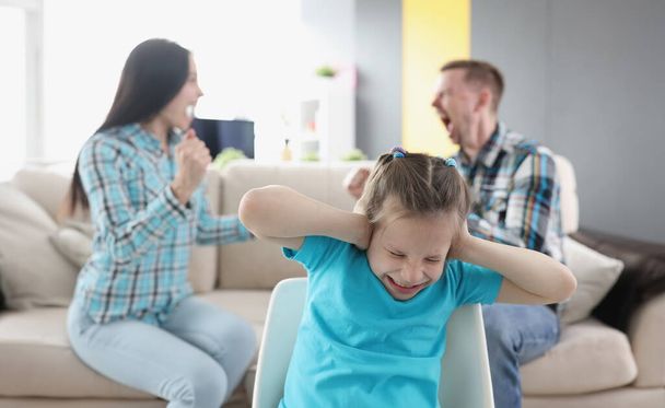 Little girl closing her ears against background of swearing parents at home. How are problems of adults reflected on child psyche concept - Photo, Image