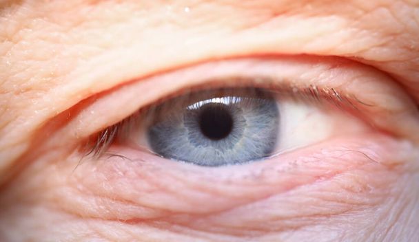 Primer plano del ojo de un anciano. Macro foto de un hombre mayor mirando en cámara. Hermoso globo ocular de color azul. Arrugas y lunares. Juventud y envejecimiento. Concepto de apariencia natural - Foto, imagen