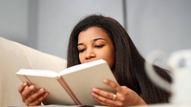 Sorridente donna nera leggere libro di storia a casa preparandosi per gli esami del college
 - Foto, immagini