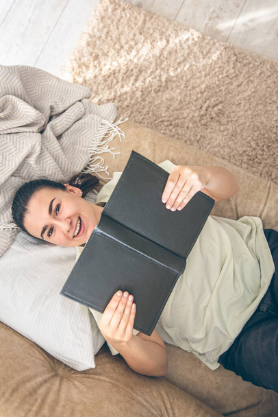 Horní pohled na šťastnou ženu ležící na pohovce ve svém útulném domě a čtení knihy, kopírovat prostor. - Fotografie, Obrázek