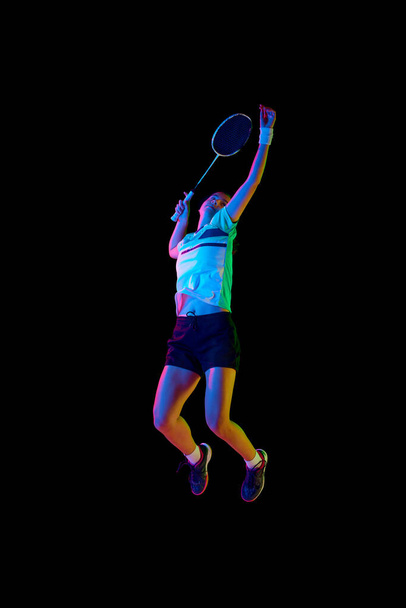 ネオンライトの黒い背景に対して動くプロの女性バドミントン選手の訓練. スポーツ,アクティブで健康的なライフスタイル,強さとパワー,アクションの概念. コピースペース. - 写真・画像