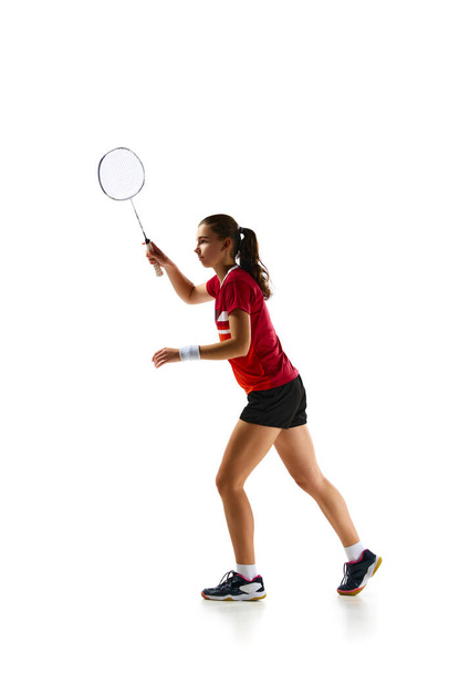 Energie en toewijding van ervaren vrouwelijke badminton speler in beweging, training vurig tegen witte studio achtergrond. Concept van sport, actieve levensstijl, kracht en kracht, actie. Kopieerruimte. - Foto, afbeelding
