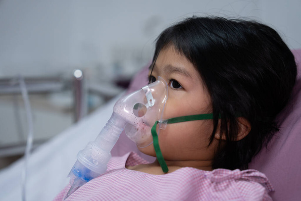 Küçük bir Asyalı kızın oksijen maskesi var ve hastanede nebulizatörle nefes alıyor. Bronşit konsepti, solunum ve tıbbi tedavi, nebulizatörden solunum ilacı, sis,. - Fotoğraf, Görsel